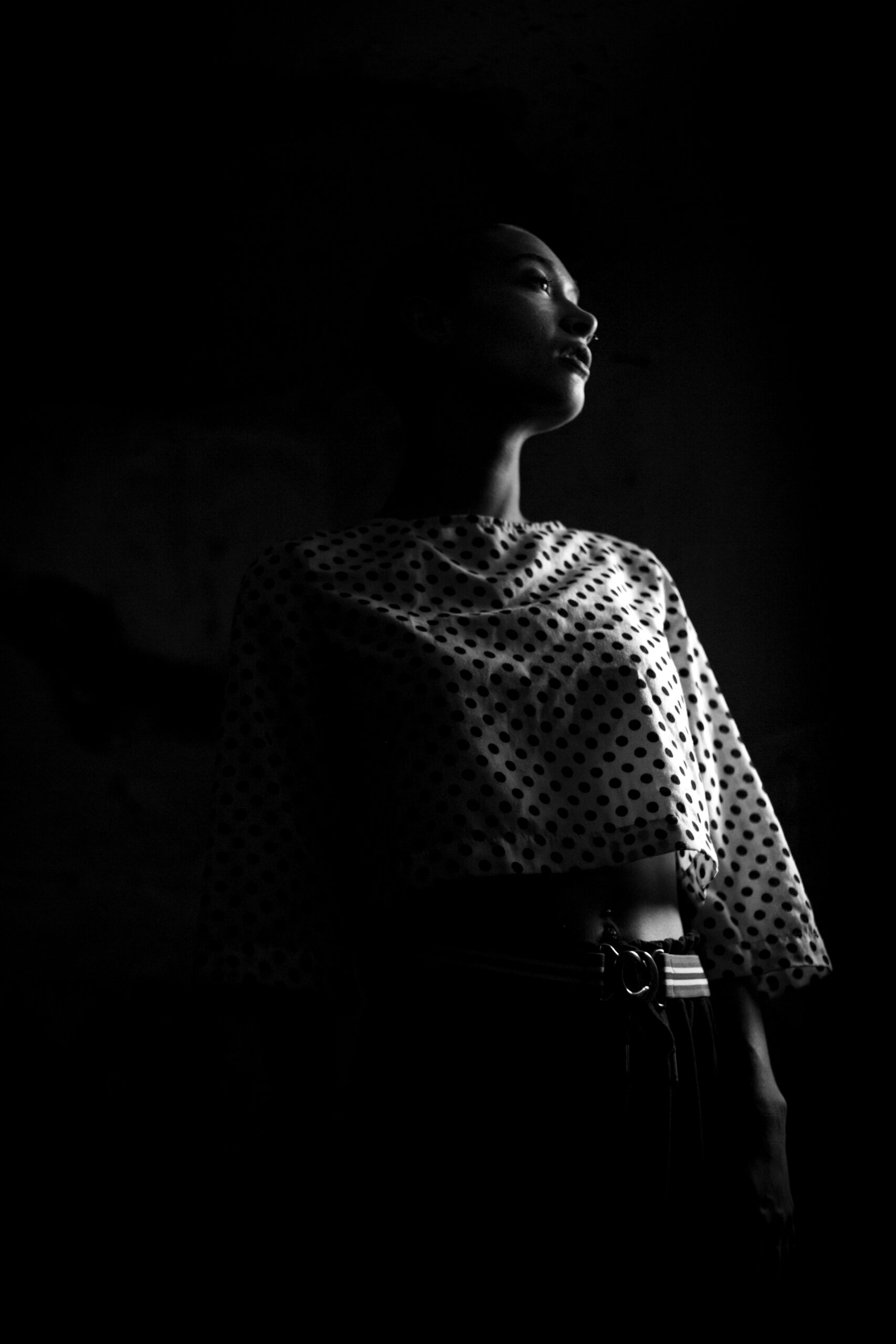 low-angle photo of woman wearing black and white polka-dot crop standing in the dark room